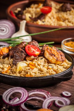 Doğu, özbek mutfağı kavramı. Biber pilav, plov bir siyah dökme demir tavada yalan malzemeler, soğan, domates, maydanoz, yanındaki ahşap bir masa üzerinde. Orta Asya mutfağı.