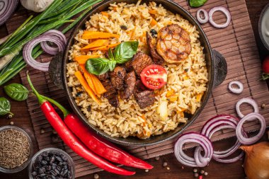 Doğu, özbek mutfağı kavramı. Biber pilav, plov bir siyah dökme demir tavada yalan malzemeler, soğan, domates, maydanoz, yanındaki ahşap bir masa üzerinde. Orta Asya mutfağı. Üstten görünüm