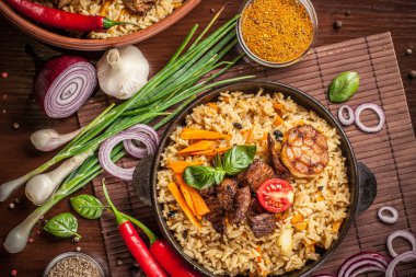 Doğu, özbek mutfağı kavramı. Biber pilav, plov bir siyah dökme demir tavada yalan malzemeler, soğan, domates, maydanoz, yanındaki ahşap bir masa üzerinde. Orta Asya mutfağı. Üstten görünüm