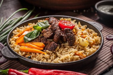 Doğu, özbek mutfağı kavramı. Biber pilav, plov bir siyah dökme demir tavada yalan malzemeler, soğan, domates, maydanoz, yanındaki ahşap bir masa üzerinde. Orta Asya mutfağı.