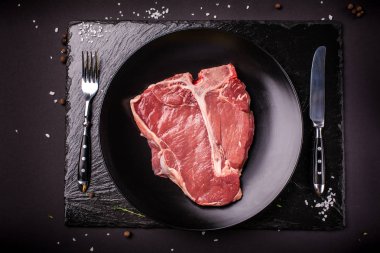 Çiğ et, sığır eti biftek, domuz eti veya dana eti, kuzu, siyah bir sayfa üzerinde siyah seramik plaka üzerinde yatıyor. Çatal ve kaşık kapatın. Üstten görünüm. Kopya alanı