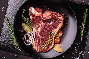 Çiğ et, sığır eti biftek, domuz eti veya dana eti, kuzu, siyah bir sayfa üzerinde siyah seramik plaka üzerinde yatıyor. Yanında et baharatlar ve sebzeler vardır. Üstten görünüm. Kopya alanı