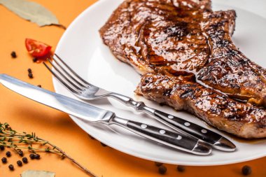 Kızarmış Kuzu biftek, Dana eti, domuz eti veya sığır eti büyük ve sulu bir parça ile baharat, çatal ve bıçak yanında beyaz seramik tabak içinde yatıyor. Üstten görünüm, kopya alanı