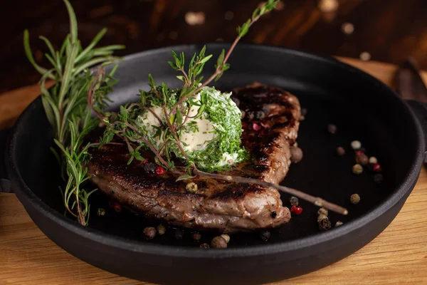 English cuisine. a large piece of a juicy steak of beef, veal, mutton or pork, lies on a cast-iron frying pan, with cream cheese and herbs, thyme, marasm.