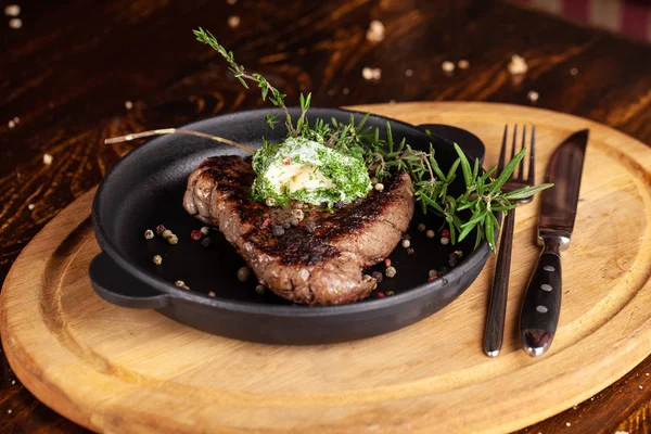 English cuisine. a large piece of a juicy steak of beef, veal, mutton or pork, lies on a cast-iron frying pan, with cream cheese and herbs, thyme, marasm.