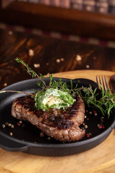 English cuisine. a large piece of a juicy steak of beef, veal, mutton or pork, lies on a cast-iron frying pan, with cream cheese and herbs, thyme, marasm.