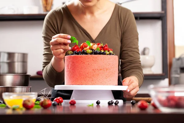 The girl, the chief confectioner, decorates forest berries, strawberries, a homemade cake made from Japanese biscuit. The concept of cooking cakes for restaurants, confectioneries. Copy space