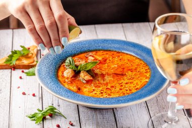 İtalyan mutfağı. Restoranda kız deniz ürünleri ve somon balık çorbası yiyor çorbanın içine kireç sıkar ve beyaz şarap içiyor. Kopya alanı, seçici odak