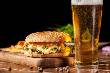 Amerikan mutfağı kavramı. Sulu hamburger eti patty, peynir ve patates kızartması bir restoranda ahşap bir gemide yalan ile. Bir bardak bira ile köpük.