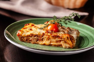 İtalyan mutfağı kavramı. Lazanya ile kıyılmış bolognese, makarna, pişmiş domates bir restoranda yeşil bir plaka üzerinde yatıyor. Bir bardak kırmızı şarap ve ekmek sepeti masaya