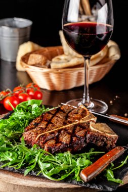 İtalyan mutfağı kavramı. Sığır eti yaşlanma sulu T-bone biftek et, rucola salata ve domates ile ihtiva eder. Bir bardak kırmızı şarap ve ekmek sepeti masaya