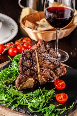 İtalyan mutfağı kavramı. Sığır eti yaşlanma sulu T-bone biftek et, rucola salata ve domates ile ihtiva eder. Bir bardak kırmızı şarap ve ekmek sepeti masaya