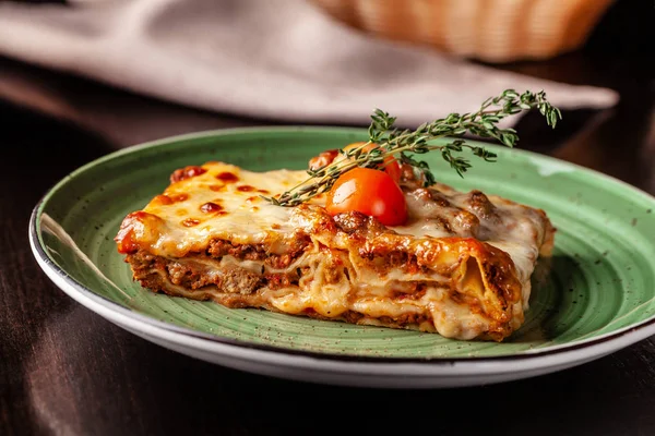 İtalyan mutfağı kavramı. Lazanya ile kıyılmış bolognese, makarna, pişmiş domates bir restoranda yeşil bir plaka üzerinde yatıyor. Bir bardak kırmızı şarap ve ekmek sepeti masaya