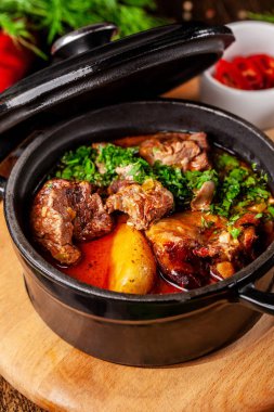 Sırp mutfağı kavramı. Kendi suyu ile patates, sebze ve Yeşiller içinde sulu pişmiş sığır eti. Ahşap bir gemide bir demir yangında hizmet.