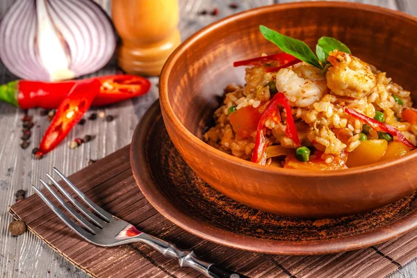 İspanya mutfağı kavramı. Paella deniz ürünleri ve karides, bir kil plaka yeşil bezelye ile. Bir kadeh iyi şarap tablodur.