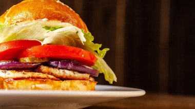 Amerikan mutfağı. Ev yapımı Hamburger tavuk fileto, domates, salatalık, kırmızı soğan, aizberg ve domates sos ile. Ülke stil patates ile. Ahşap bir masaya.