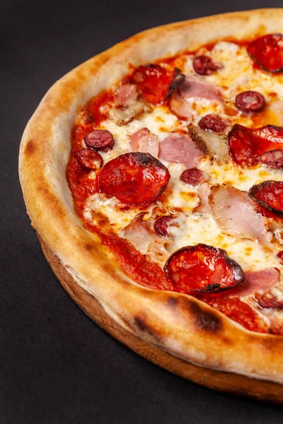 The concept of Italian cuisine. Real Italian pizza on a thin cake with large sides on a black background. Close up. Background image.