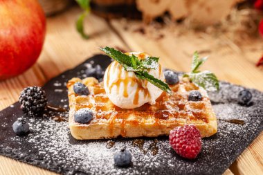 Bir kepçe dondurma, taze çilek ahududu, böğürtlen, yaban mersini ve nane ile Belçika Waffle. Krema şeker ile silkeledi ve karamel sos dökülür. seçici odak