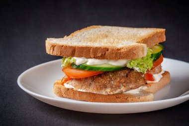 Ev yapımı ekmek ekmek, kızarmış yumurta, eritilmiş peynir, domates, salatalık, marul, hamburger ve mayonez sos hazırladım. Siyah bir arka plan üzerinde beyaz bir plaka üzerinde sandviç.