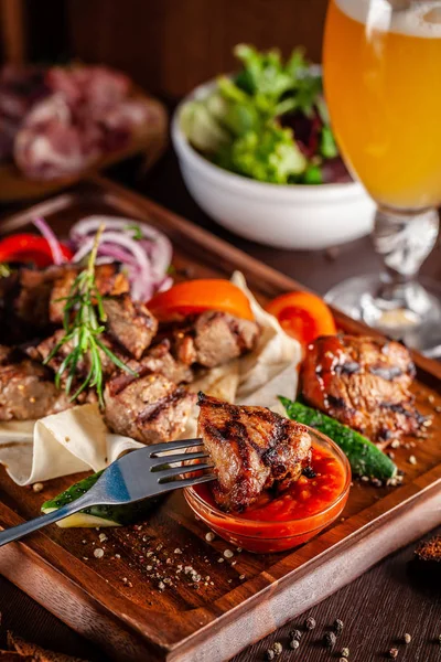 Gürcü mutfağı kavramı. Sığır eti, domuz eti ve tavuk kebap ile büyük bir ahşap tahta. Barbekü sos ve ketçap. Arka planda bir light bira köpük bardak
