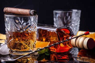 alkolizm kavramı, yalnızlık, bağımlılık. Bir şişe viski, bir bardak viski ve buzlu, siyah bir masada dumanlı bir puro, siyah bir arka plan üzerinde. Erkeksi rahatlama için elit içecek