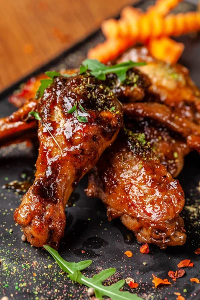 The concept of Indian cuisine. Baked chicken wings and legs in honey mustard sauce. Serving dishes in the restaurant on a black plate. Indian spices on a wooden table. background image.