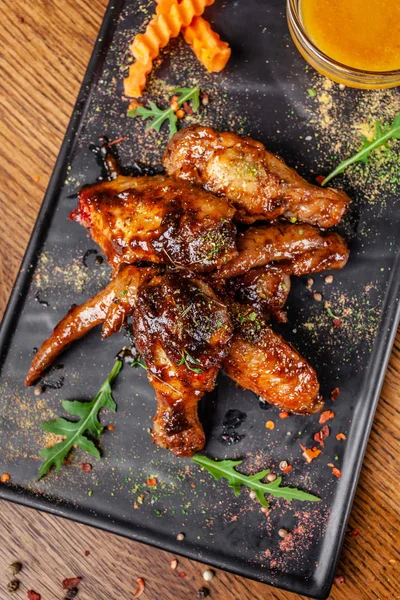 The concept of Indian cuisine. Baked chicken wings and legs in honey mustard sauce. Serving dishes in the restaurant on a black plate. Indian spices on a wooden table. background image.