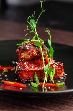 Amerikan mutfağı kavramı. Domuz kaburga, pişmiş ve barbekü sosuna sırlı kavrulmuş. Siyah plaka restoran yemekleri susam ve mikro ile yeşil hizmet. Bir bardak kırmızı şarap yanında.