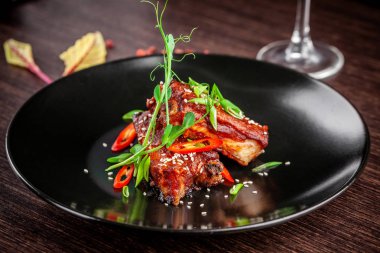 Amerikan mutfağı kavramı. Domuz kaburga, pişmiş ve barbekü sosuna sırlı kavrulmuş. Siyah plaka restoran yemekleri susam ve mikro ile yeşil hizmet. Bir bardak kırmızı şarap yanında.