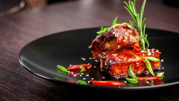 美国美食的概念 烤猪肉排骨 烤和上釉烧烤酱 餐厅的菜肴放在一个黑色的盘子里 配上芝麻和微绿色 旁边有一杯红酒 — 图库照片