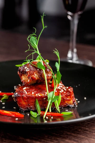 Amerikan mutfağı kavramı. Domuz kaburga, pişmiş ve barbekü sosuna sırlı kavrulmuş. Siyah plaka restoran yemekleri susam ve mikro ile yeşil hizmet. Bir bardak kırmızı şarap yanında.