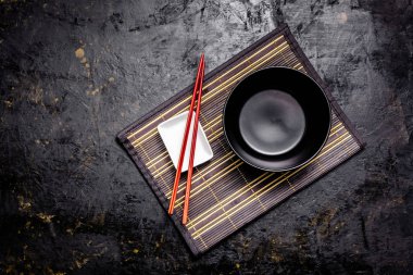 Boş Japon yemekleri. Çin noodle veya Tay çorba için siyah seramik kase bamkuk halıya yatıyor. Soya sosu ve kırmızı Çin için beyaz saucepot bir siyah arka plan üzerine yapışır. Üstten görünüm, kopya alanı