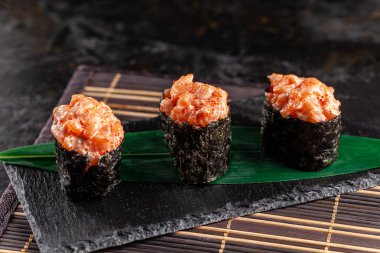 Somon bir bambu yaprak ve siyah taş mazisi ile gunkan Maki Sushi ile. Bambu hasır. kırmızı Çin sopa. Sushi Menüsü. Japon yemekleri. eğilim renk 2019 mercan. arka plan resmi