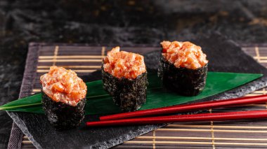 Somon bir bambu yaprak ve siyah taş mazisi ile gunkan Maki Sushi ile. Bambu hasır. kırmızı Çin sopa. Sushi Menüsü. Japon yemekleri. eğilim renk 2019 mercan. arka plan resmi