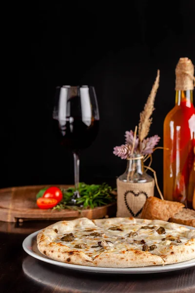 The concept of Italian cuisine. Thin cheese pizza with mushrooms, with large sides of Semola flour. A string of red wine on the table. Serving dishes in the restaurant