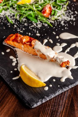 İtalyan mutfağı kavramı. Roka, domates ve parmesan peyniri kremalı limon soslu somon fileto. Bir bardak beyaz şarap masanın üzerinde. Restoranda yemeklerin.
