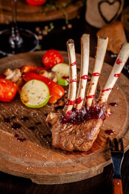 Rack Kuzu ızgara sebzeler ve frambuaz sos ile. Yemekler bir ahşap tahta üzerinde hizmet veren bir kadeh kırmızı şarap ile. Güzel yemek restoran. Arka plan görüntüsü. kopya alanı