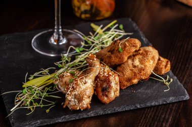 İtalyan mutfağı kavramı. Bira için snack. Sırlı tavuk budu ve tavuk kanatları, tava. Siyah taş mazisi üzerine restoran yemekleri sunan. Kopya alanı
