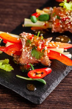 Avrupa mutfağı kavramı. Aperatif şarap için. Çiğ Dana rulo gevrek sebzeler, salatalık, kereviz, kırmızı dolmalık biber ile. Siyah bir taş kayrak tahtada restoranda yemekler sunan