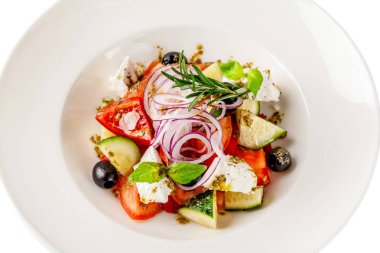 Yunan mutfağı kavramı. Salata domates, salatalık, biber, zeytin ve beyaz peynir. zeytin yağı ile giyinmiş ve taze fesleğen ile dekore edilmiştir. Beyaz bir arka plan üzerinde beyaz tabak.