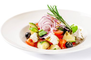 Yunan mutfağı kavramı. Salata domates, salatalık, biber, zeytin ve beyaz peynir. zeytin yağı ile giyinmiş ve taze fesleğen ile dekore edilmiştir. Beyaz bir arka plan üzerinde beyaz tabak.