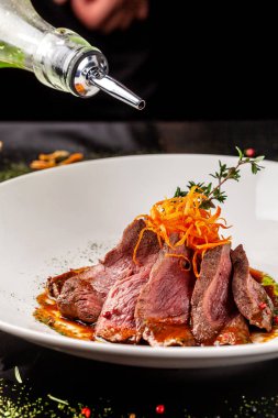 Avrupa mutfağı. Orta pişmiş rosto ile marine edilmiş Dana. Kavurma derecesi. Şef sığır eti zeytinyağı dökülen. Beyaz bir plaka restoran yemekleri sunan. arka plan resmi, kopya alanı