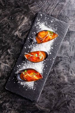 Avrupa mutfağı. Biberiye, sarımsak, biber domates soslu Marine midye. Siyah bir arka plan üzerine kaba deniz tuzu ile bir plaka üzerinde restoranda yemekler sunan. kopya alanı