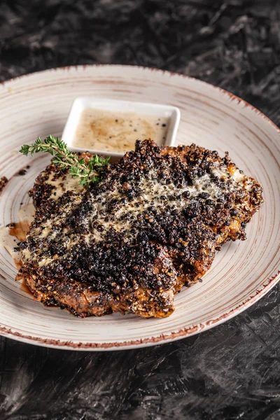 The concept of American cuisine. Fried, juicy pork steak in black pepper with thyme and white cheese sauce on a white ceramic dish. Serving dishes in the restaurant. copy space — Stock Photo, Image