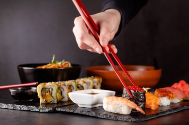 Japon mutfağı kavramı. Bir kız kırmızı Çin yemek çubukları tutar ve bir restoranda yemek suşi. arka plan görüntüsü. Popüler Japon yemekleri. kopya alanı