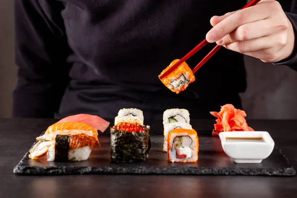 The concept of Japanese cuisine. A girl holds a red Chinese chopsticks and eat sushi in a restaurant. background image. Popular Japanese food. copy space