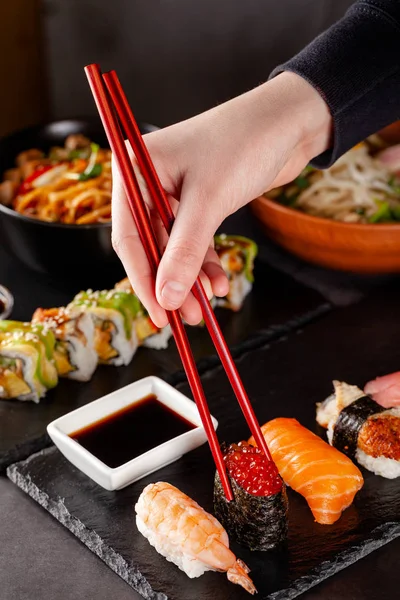 The concept of Japanese cuisine. A girl holds a red Chinese chopsticks and eat sushi in a restaurant. background image. Popular Japanese food. copy space