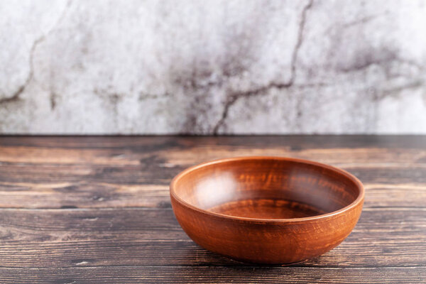 An empty plate of red clay stands on a wooden table, copy space