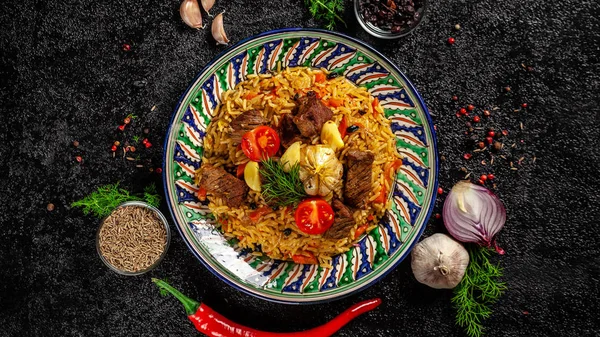 O conceito de cozinha oriental. Pilaf uzbeque nacional com carne em uma frigideira de ferro fundido, em uma mesa de madeira. imagem de fundo. vista superior, espaço de cópia, leigos planos — Fotografia de Stock