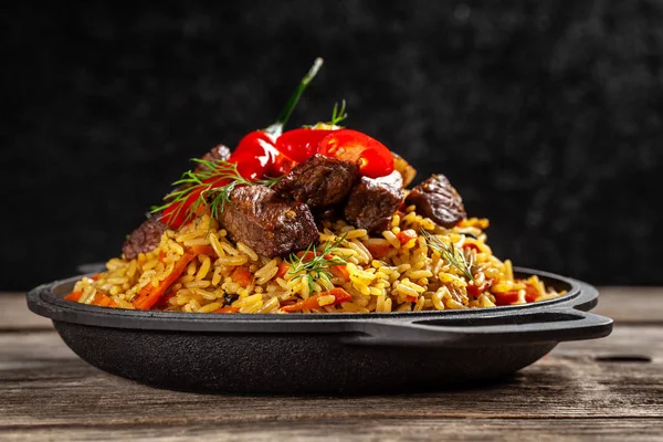 Doğu mutfağı kavramı. Ulusal Özbek pilavı ile ahşap bir masa üzerinde bir dökme demir tavada et. arka plan görüntüsü. görünümü ana sayfa, yer kopyalayın, yat